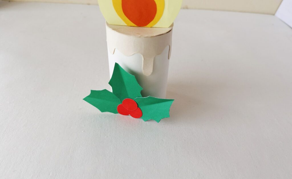 Paper holly and berries being added to the front of the paper candle.