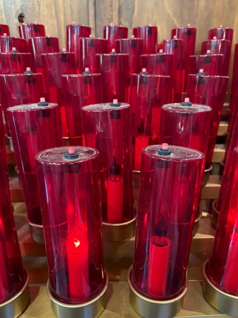 Red votive candles burning in prayer at a Catholic pilgrimage site.