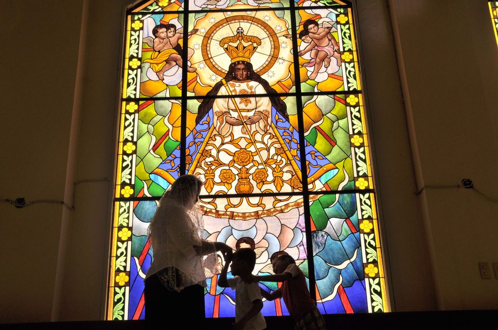 Children standing in front of a colorful stained-glass window in a Catholic church