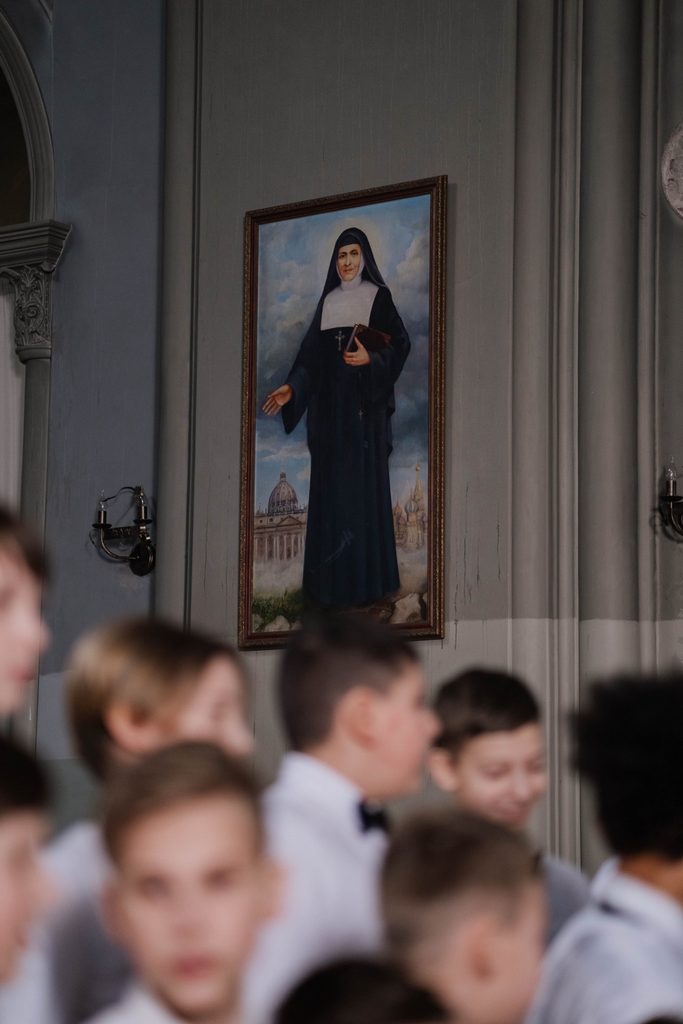 Portrait of a Catholic saint hanging above children gathered in a church